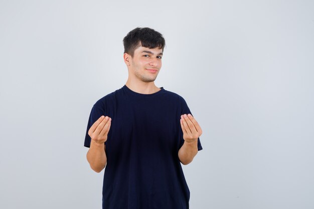 Jonge man doet Italiaans gebaar in zwart t-shirt en kijkt zelfverzekerd, vooraanzicht.