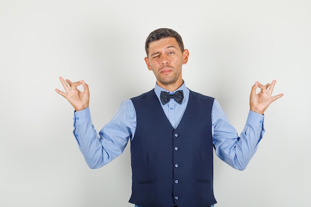 Jonge man doet meditatie gebaar met vingers in pak en kijkt ontspannen. vooraanzicht.