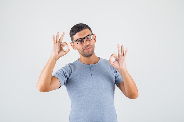 Jonge man doet ok teken met vingers in grijs t-shirt, bril en op zoek tevreden