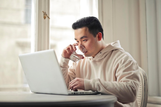 jonge man drinkt een glas water en werkt met computer