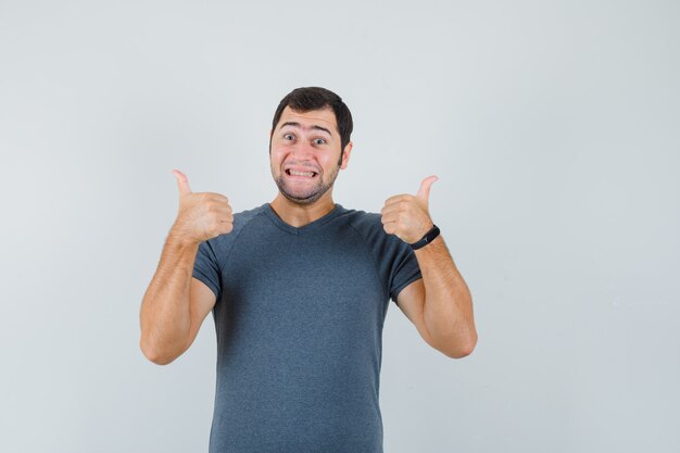 Jonge man dubbele duimen opdagen in grijs t-shirt en vrolijk kijken