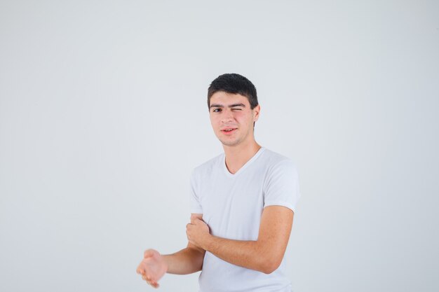 Jonge man een oog sluiten terwijl hij naar de camera in een t-shirt kijkt en er grappig uitziet. vooraanzicht.