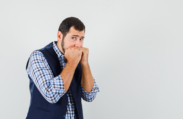 Jonge man emotioneel vuisten bijten in shirt, vest en op zoek bang, vooraanzicht.