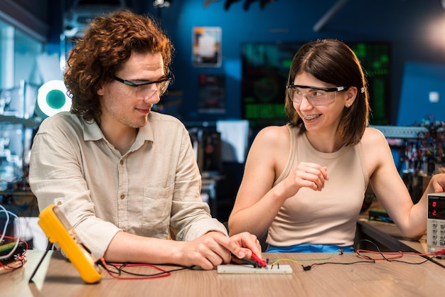 Gratis foto jonge man en vrouw in beschermende bril doen experimenten met elektriciteit in een laboratorium