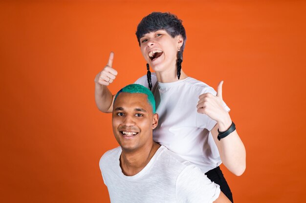 Jonge man en vrouw in casual wit op oranje muur, blije en positieve emoties tonen duim omhoog