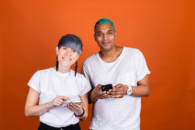 Jonge man en vrouw in casual wit op oranje muur met mobiele telefoon gelukkig samen glimlach