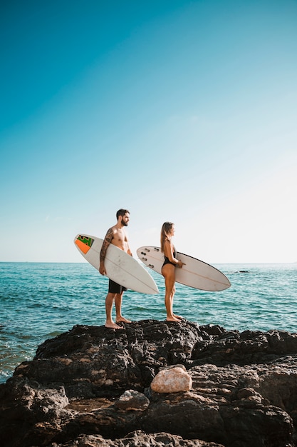 Jonge man en vrouw met surfplanken op steen in de buurt van zee