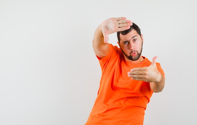 Jonge man frame gebaar maken in oranje t-shirt en op zoek naar vertrouwen. vooraanzicht.