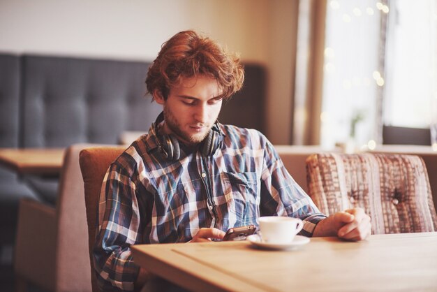 Jonge man freelancer met een baard in alledaagse kleding zitten in een café met een kopje koffie