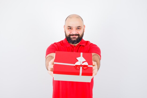Jonge man geeft cadeau in rood shirt en ziet er geliefd uit, vooraanzicht.