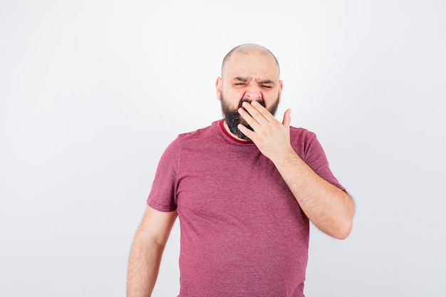 Jonge man geeuwt in roze t-shirt en ziet er moe uit. vooraanzicht.