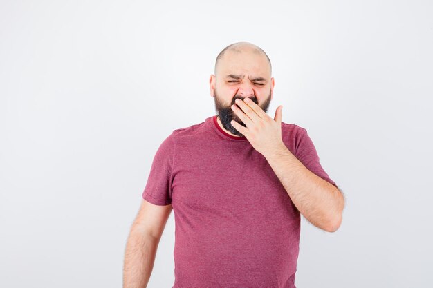 Jonge man geeuwt in roze t-shirt en ziet er moe uit. vooraanzicht.