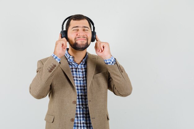 Jonge man genieten van muziek met koptelefoon in shirt, jasje en rustig kijken. vooraanzicht.