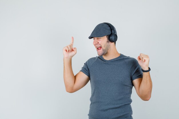 Jonge man genieten van muziek met koptelefoon in t-shirt, pet en op zoek dartel, vooraanzicht.