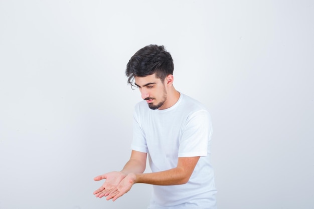 Jonge man hand in hand in biddend gebaar in wit t-shirt en hoopvol kijkend