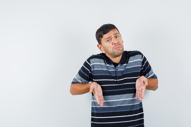 Jonge man hand in hand zoals iets hieronder in t-shirt laten zien en verward kijken. vooraanzicht.