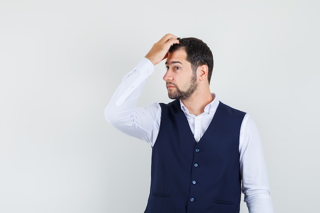 Jonge man haren kammen met vingers in shirt, vest en stijlvol op zoek