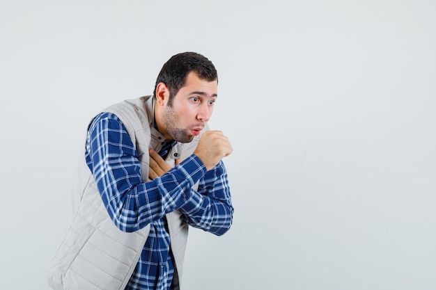 Jonge man hoesten in shirt, mouwloos jasje en ziek, vooraanzicht kijken. ruimte voor tekst