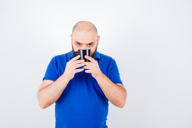 Jonge man houdt beker vast terwijl hij naar de camera in blauw shirt kijkt en gefocust kijkt, vooraanzicht.