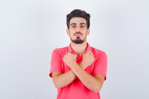 Jonge man houdt gekruiste vuisten op de borst in een t-shirt en ziet er zelfverzekerd uit, vooraanzicht.