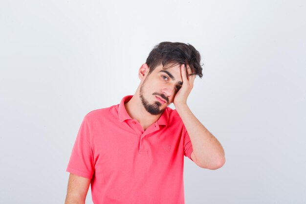 Jonge man houdt hand op gezicht in roze t-shirt en kijkt peinzend. vooraanzicht.