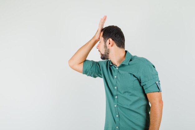 Jonge man houdt hand op zijn voorhoofd in groen shirt en kijkt ontevreden, vooraanzicht.
