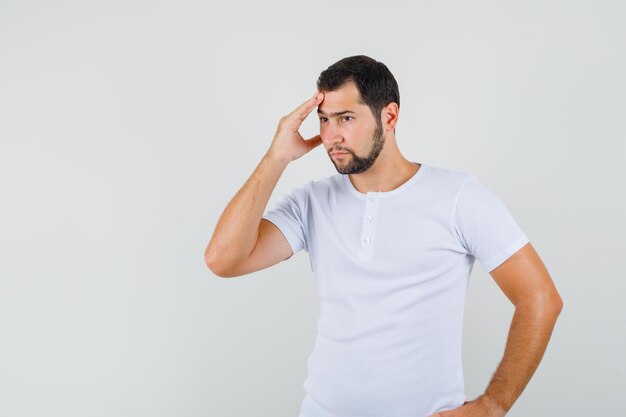 Jonge man houdt hand op zijn voorhoofd in t-shirt en kijkt bezorgd. vooraanzicht.