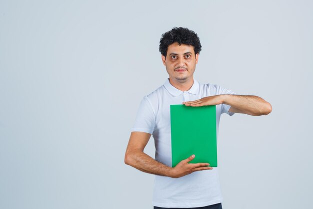 Jonge man houdt klembord in wit t-shirt, broek en ziet er elegant uit. vooraanzicht.