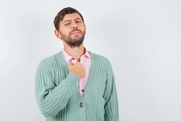 Jonge man houdt vuist op borst in shirt, vest en ziet er trots uit. vooraanzicht.