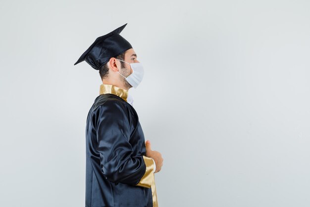 Jonge man in afgestudeerde uniform houdt zijn jurk vast en kijkt attent.