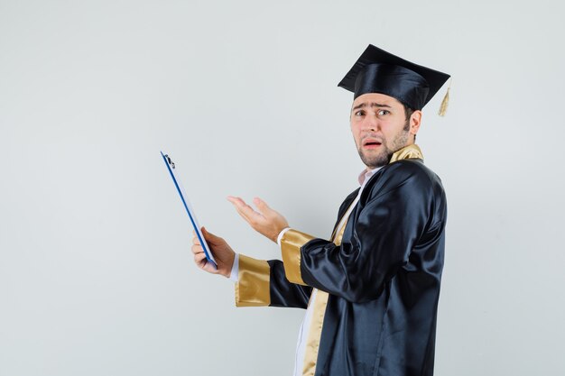 Jonge man in afgestudeerde uniform klembord te houden en op zoek naar onrust.