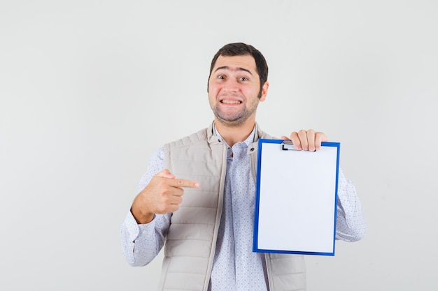 Jonge man in beige jas wijst naar notebook met wijsvinger en kijkt optimistisch, vooraanzicht.