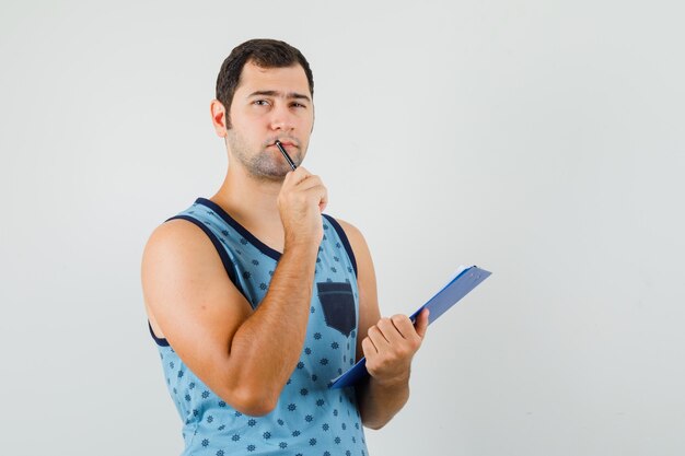 Jonge man in blauw hemd met klembord en pen en peinzend op zoek