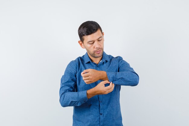 Jonge man in blauw shirt dichtknopen op de mouw van zijn shirt en op zoek voorzichtig, vooraanzicht.