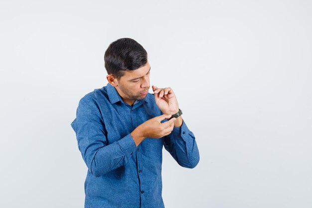 Jonge man in blauw shirt die horloge draagt en er voorzichtig uitziet, vooraanzicht.