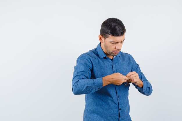 Jonge man in blauw shirt die horloge probeert te dragen en er voorzichtig uitziet, vooraanzicht.