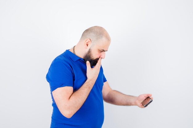 Jonge man in blauw shirt die naar de telefoon kijkt en angstig kijkt.