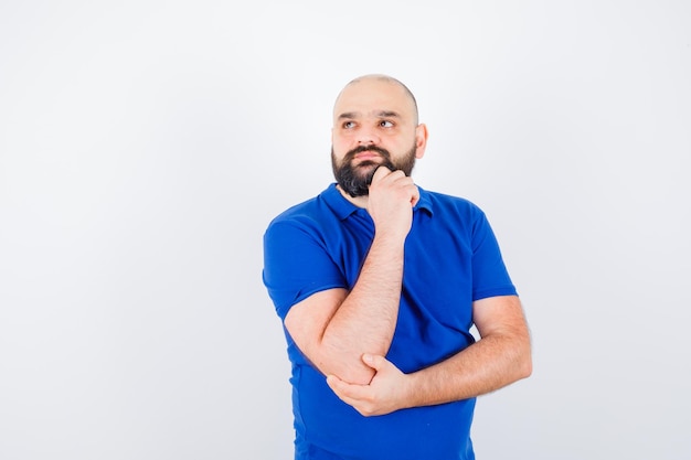 Jonge man in blauw shirt die wegkijkt en attent kijkt, vooraanzicht.