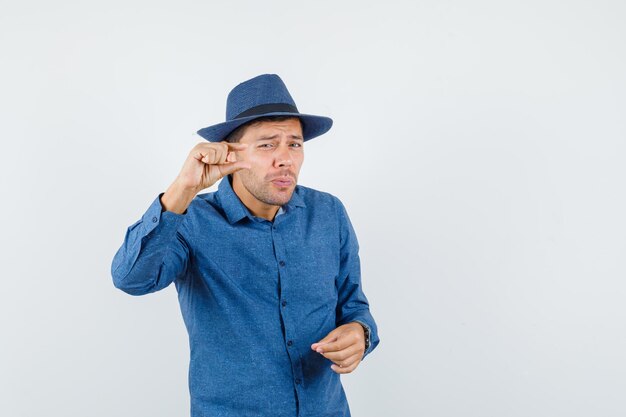 Jonge man in blauw shirt, hoed met klein bordje, vooraanzicht.