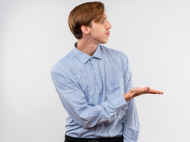 Jonge man in blauw shirt iets presenteren met arm van zijn hand opzij kijken staande over witte muur