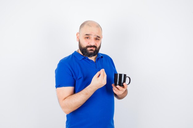 Jonge man in blauw shirt met beker terwijl hij een heerlijk gebaar toont, vooraanzicht.