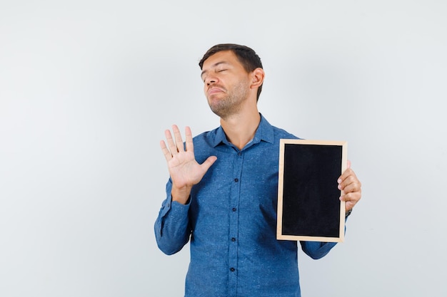 Jonge man in blauw shirt met schoolbord zonder gebaar en geestloos, vooraanzicht.