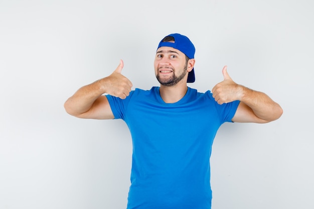 Jonge man in blauw t-shirt en pet duimen opdagen en tevreden kijken