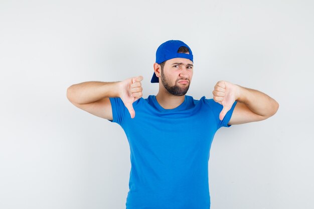 Jonge man in blauw t-shirt en pet met duimen naar beneden en ontevreden op zoek
