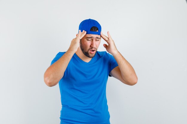 Jonge man in blauw t-shirt en pet met hoofdpijn en op zoek moe