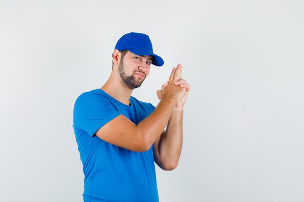 Jonge man in blauw t-shirt en pet met pistool gebaar schieten en glimlachen