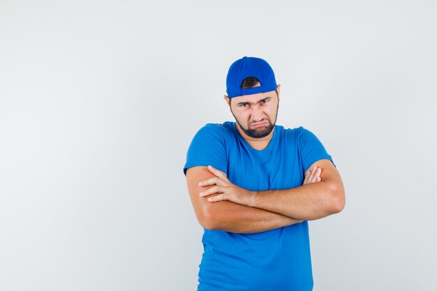 Jonge man in blauw t-shirt en pet staan met gekruiste armen en kijken beledigd