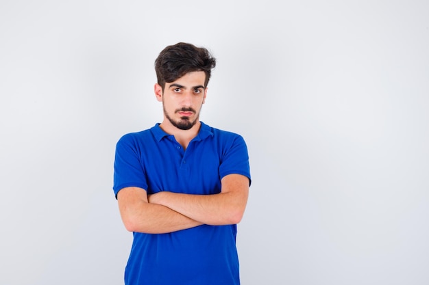 Jonge man in blauw t-shirt staande armen gekruist en serieus kijkend