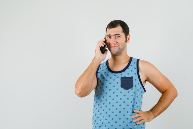 Jonge man in blauwe hemd praten op mobiele telefoon en vrolijk kijken