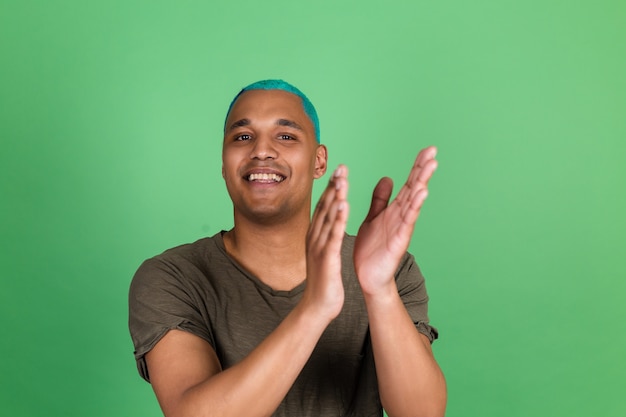 Jonge man in casual op groene muur blauw haar gelukkige positieve glimlach op zoek naar camera en juicht gefeliciteerd!